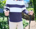 Person outdoors holding two black trekking poles with foam grips, ready for a hike.