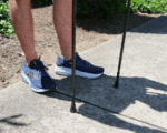 Person wearing blue athletic shoes standing on a concrete path with two crutches planted beside their feet.
