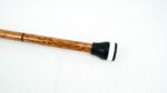 Wooden walking stick with a black rubber end cap on a white surface, lying diagonally across the image.